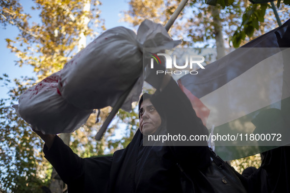 A veiled Iranian woman stands in front of a Palestinian flag while holding a package wrapped in a shroud, symbolizing the body of a Palestin...