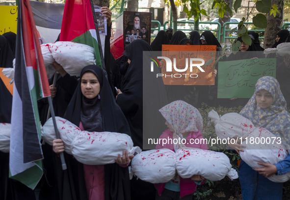 A veiled Iranian woman holds an anti-UN placard, while young girls hold packages wrapped in shrouds, symbolizing the bodies of Palestinian a...