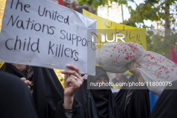 A veiled Iranian woman holds an anti-UN placard, while another woman holds up a package wrapped in a shroud, symbolizing the body of a Leban...