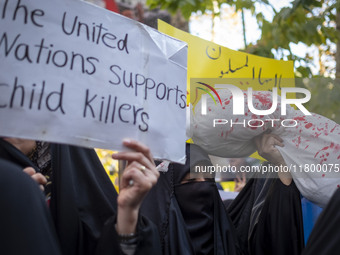 A veiled Iranian woman holds an anti-UN placard, while another woman holds up a package wrapped in a shroud, symbolizing the body of a Leban...