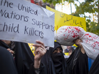 A veiled Iranian woman holds an anti-UN placard, while another woman holds up a package wrapped in a shroud, symbolizing the body of a Leban...