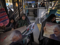 Veiled Iranian women hold an anti-U.S., anti-British, and anti-Israeli placard, along with portraits of the former commander of the Islamic...