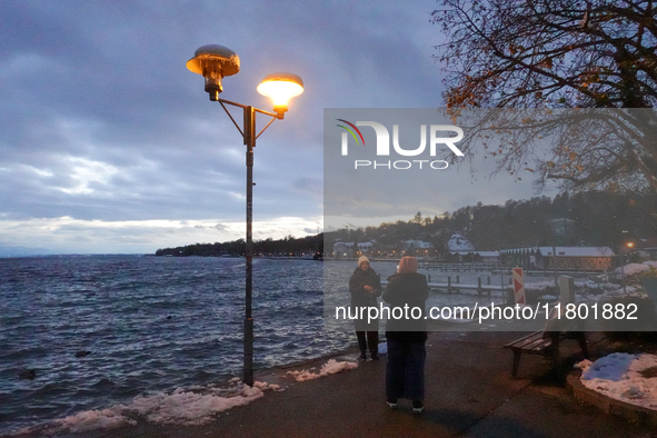 This waterfront promenade of Lake Starnberg in Germany, on November 22, 2024, is illuminated by a glowing streetlight that gently brightens...