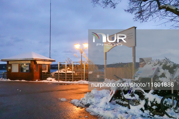 The Lake Starnberg waterfront promenade, adorned with fresh snow, creates a tranquil scene under the warm glow of streetlights in Lake Starn...