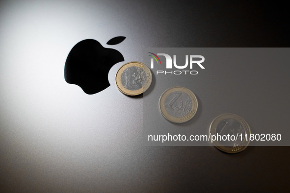 An Apple logo is on the back of a MacBook next to three Euro coins in Athens, Greece, on November 23, 2024. 