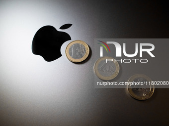 An Apple logo is on the back of a MacBook next to three Euro coins in Athens, Greece, on November 23, 2024. (