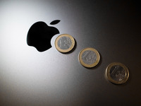 An Apple logo is on the back of a MacBook next to three Euro coins in Athens, Greece, on November 23, 2024. (