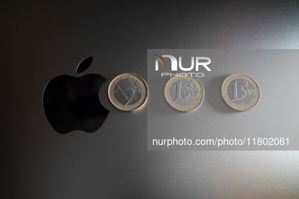 An Apple logo is on the back of a MacBook next to three Euro coins in Athens, Greece, on November 23, 2024. 