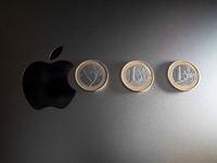 An Apple logo is on the back of a MacBook next to three Euro coins in Athens, Greece, on November 23, 2024. (