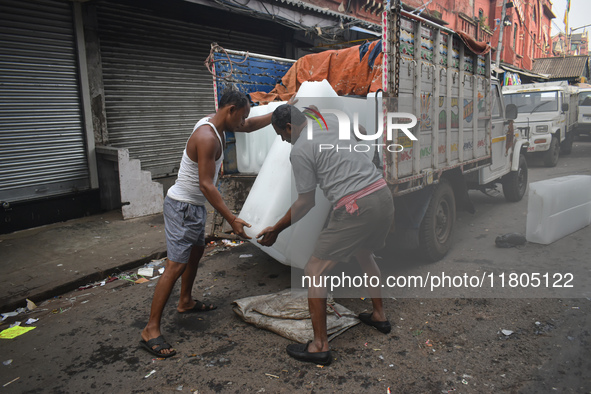 Labourers unload a large ice block from a truck inside a wholesale market in Kolkata, India, on November 24, 2024. 