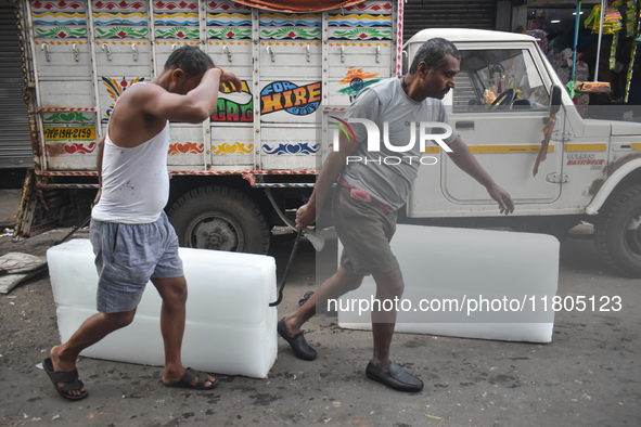 Labourers unload a large ice block from a truck inside a wholesale market in Kolkata, India, on November 24, 2024. 