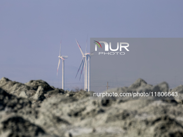 Power windmills are seen behind an austere, harsh landscape of dry mud left on mud volcano in Gobustan region near Baku, Azerbaijan on Novem...