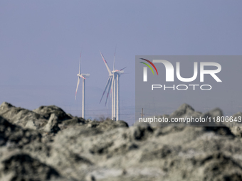 Power windmills are seen behind an austere, harsh landscape of dry mud left on mud volcano in Gobustan region near Baku, Azerbaijan on Novem...