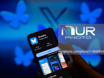 The Bluesky app logo is displayed on a smartphone with the Bluesky icon together with X visible in the background in this photo illustration...