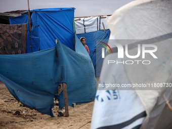 A displaced Palestinian girl stands in front of her family's tent, which is damaged by wind and rain after heavy rainfall in Deir al-Balah,...