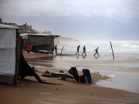 Displaced Palestinian boys walk along the seashore outside their tents, which are damaged by wind and rain following heavy rainfall in Deir...