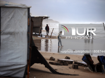 Displaced Palestinian boys walk along the seashore outside their tents, which are damaged by wind and rain following heavy rainfall in Deir...