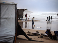 Displaced Palestinian boys walk along the seashore outside their tents, which are damaged by wind and rain following heavy rainfall in Deir...