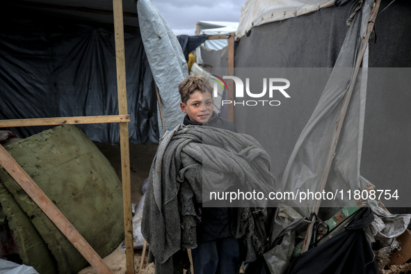 A displaced Palestinian boy carries a blanket in front of his family's tent, which is damaged by wind and rain following heavy rainfall in D...