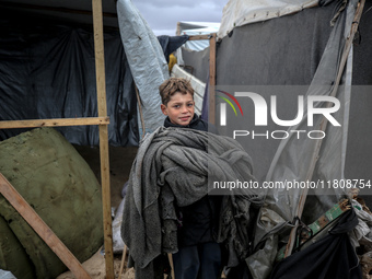 A displaced Palestinian boy carries a blanket in front of his family's tent, which is damaged by wind and rain following heavy rainfall in D...