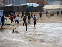 Displaced Palestinian boys walk along the seashore outside their tents, which are damaged by wind and rain following heavy rainfall in Deir...