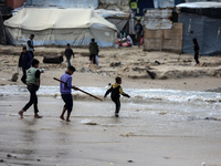 Displaced Palestinian boys walk along the seashore outside their tents, which are damaged by wind and rain following heavy rainfall in Deir...