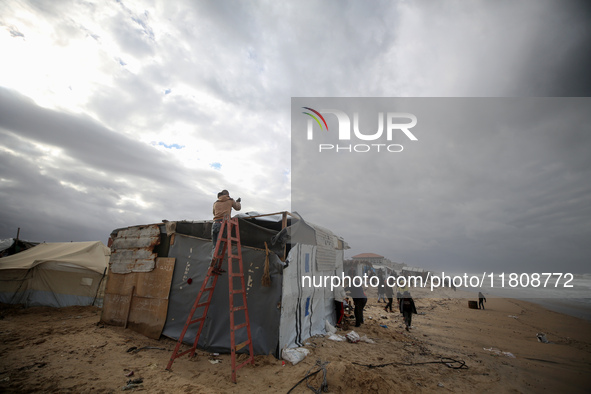 A displaced Palestinian man tries to fix a wind and rain-damaged tent following heavy rainfall in Deir al-Balah, central Gaza Strip, on Nove...