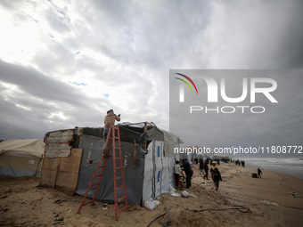 A displaced Palestinian man tries to fix a wind and rain-damaged tent following heavy rainfall in Deir al-Balah, central Gaza Strip, on Nove...