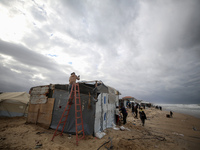 A displaced Palestinian man tries to fix a wind and rain-damaged tent following heavy rainfall in Deir al-Balah, central Gaza Strip, on Nove...