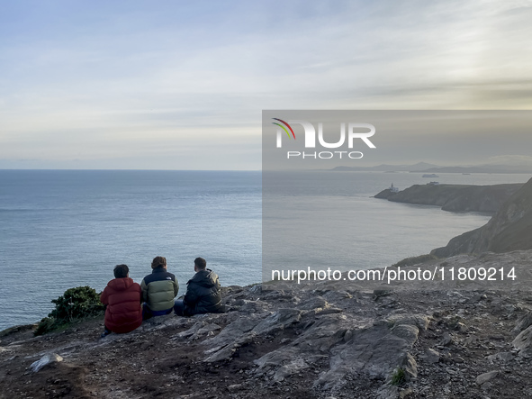 Three men look at the lighthouse on the Howth Cliff Walk in Howth, Ireland, in November 2024 