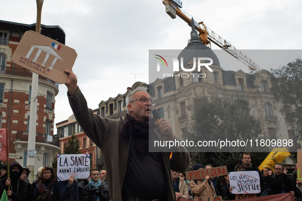 An opponent speaks with a placard depicting the French National Assembly. People gather in Toulouse, France, on November 25, 2024, as plaint...