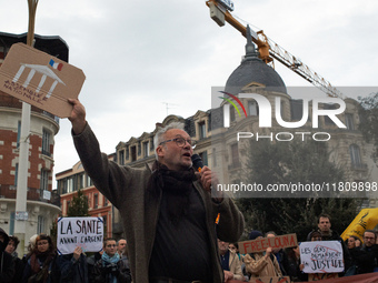 An opponent speaks with a placard depicting the French National Assembly. People gather in Toulouse, France, on November 25, 2024, as plaint...