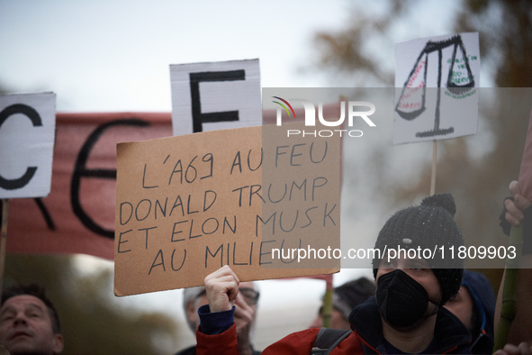 A man holds a placard reading 'A69 in the fire, Donald Trump and Elon Musk in the middle'. People gather in Toulouse, France, on November 25...