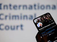 Benjamin Netanyahu's social media is displayed on a smartphone with the International Criminal Court visible in the background in this photo...