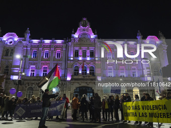 Demonstrators carry signs saying no more violence against women and a Palestinian flag as they walk past the town hall, which is lit up in p...