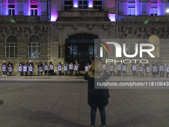 Demonstrators with signs reading ''They are not dead, they are murdered'' pose in front of the town hall illuminated in purple for the demon...