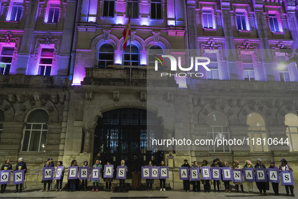 Demonstrators with signs reading ''They are not dead, they are murdered'' pose in front of the town hall illuminated in purple for the demon...