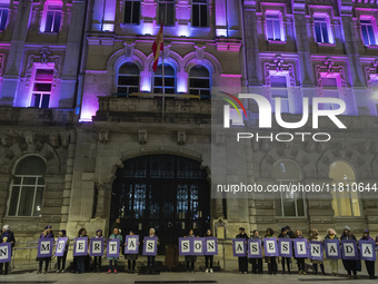 Demonstrators with signs reading ''They are not dead, they are murdered'' pose in front of the town hall illuminated in purple for the demon...