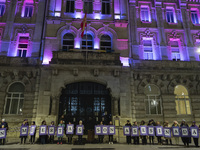 Demonstrators with signs reading ''They are not dead, they are murdered'' pose in front of the town hall illuminated in purple for the demon...