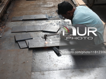 A laborer cuts an iron plate outside a shop at a steel and iron wholesale market in Kolkata, India, on November 26, 2024. In November 2024,...