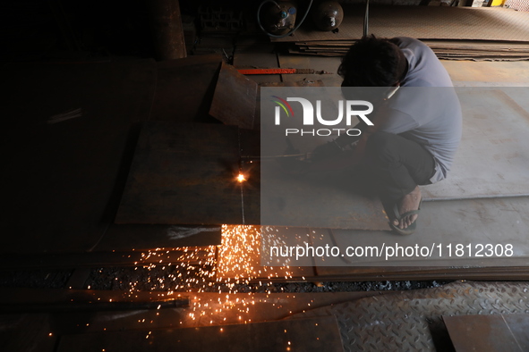 A laborer cuts an iron plate outside a shop at a steel and iron wholesale market in Kolkata, India, on November 26, 2024. In November 2024,...