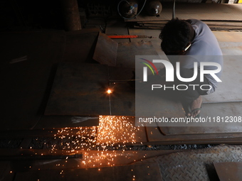 A laborer cuts an iron plate outside a shop at a steel and iron wholesale market in Kolkata, India, on November 26, 2024. In November 2024,...