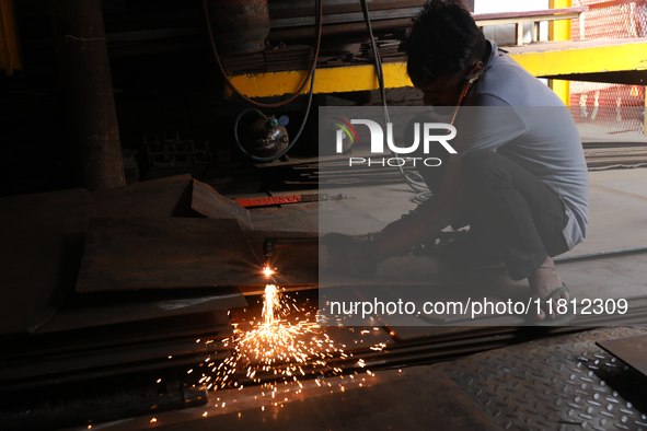 A laborer cuts an iron plate outside a shop at a steel and iron wholesale market in Kolkata, India, on November 26, 2024. In November 2024,...