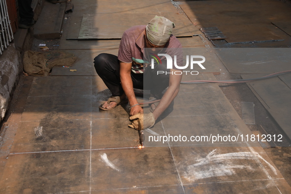 A laborer works with an iron plate outside a shop at a steel and iron wholesale market in Kolkata, India, on November 26, 2024. In November...