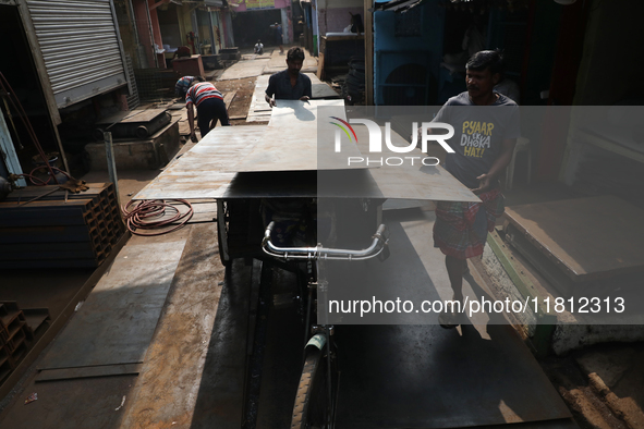 Labourers carry an iron plate to load onto a cycle rickshaw outside a shop at a steel and iron wholesale market in Kolkata, India, on Novemb...