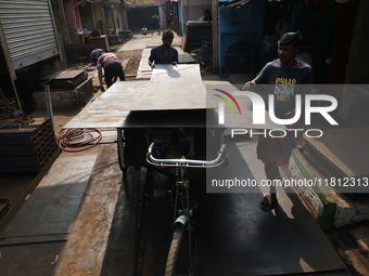 Labourers carry an iron plate to load onto a cycle rickshaw outside a shop at a steel and iron wholesale market in Kolkata, India, on Novemb...