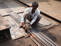 A laborer cuts iron rods outside a shop at a steel and iron wholesale market in Kolkata, India, on November 26, 2024. In November 2024, Indi...