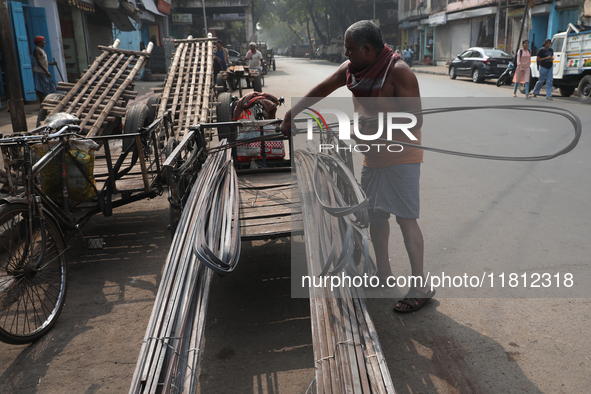 A laborer loads iron rods onto a cycle rickshaw outside a shop at a steel and iron wholesale market in Kolkata, India, on November 26, 2024....