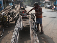 A laborer loads iron rods onto a cycle rickshaw outside a shop at a steel and iron wholesale market in Kolkata, India, on November 26, 2024....