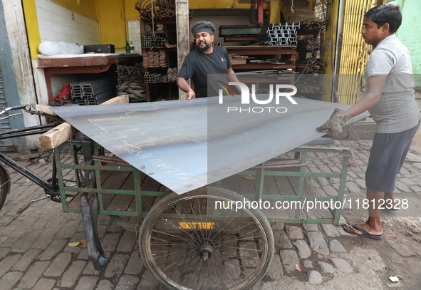 Labourers carry an iron plate to load onto a cycle rickshaw outside a shop at a steel and iron wholesale market in Kolkata, India, on Novemb...